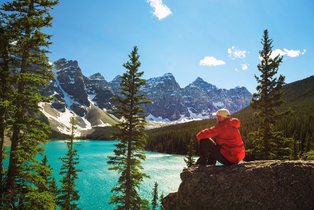 Hiker enjoying the view of Moraine lake in Banff National Park, Alberta, Canada, with snow-covered peaks of Canadian Rocky Mountains in the background